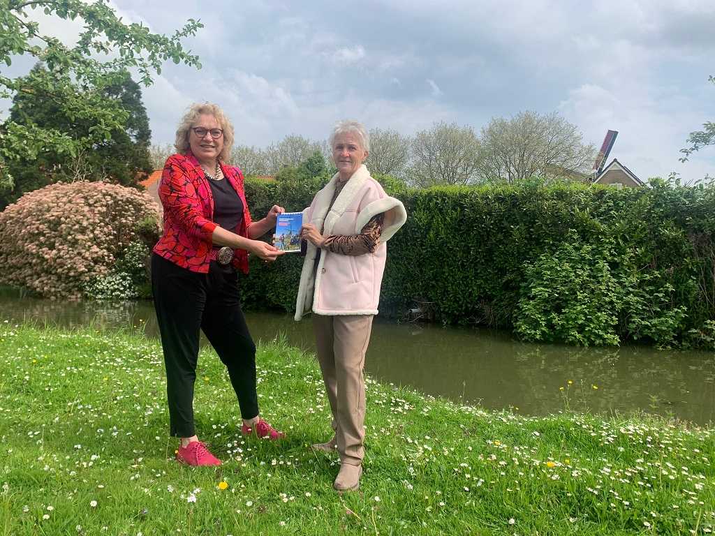 Anastasia van der Lugt en Margot Stolk schudden handen tijdens de overhandiging van de Wandelgids Oude Hollandse Waterlinie.